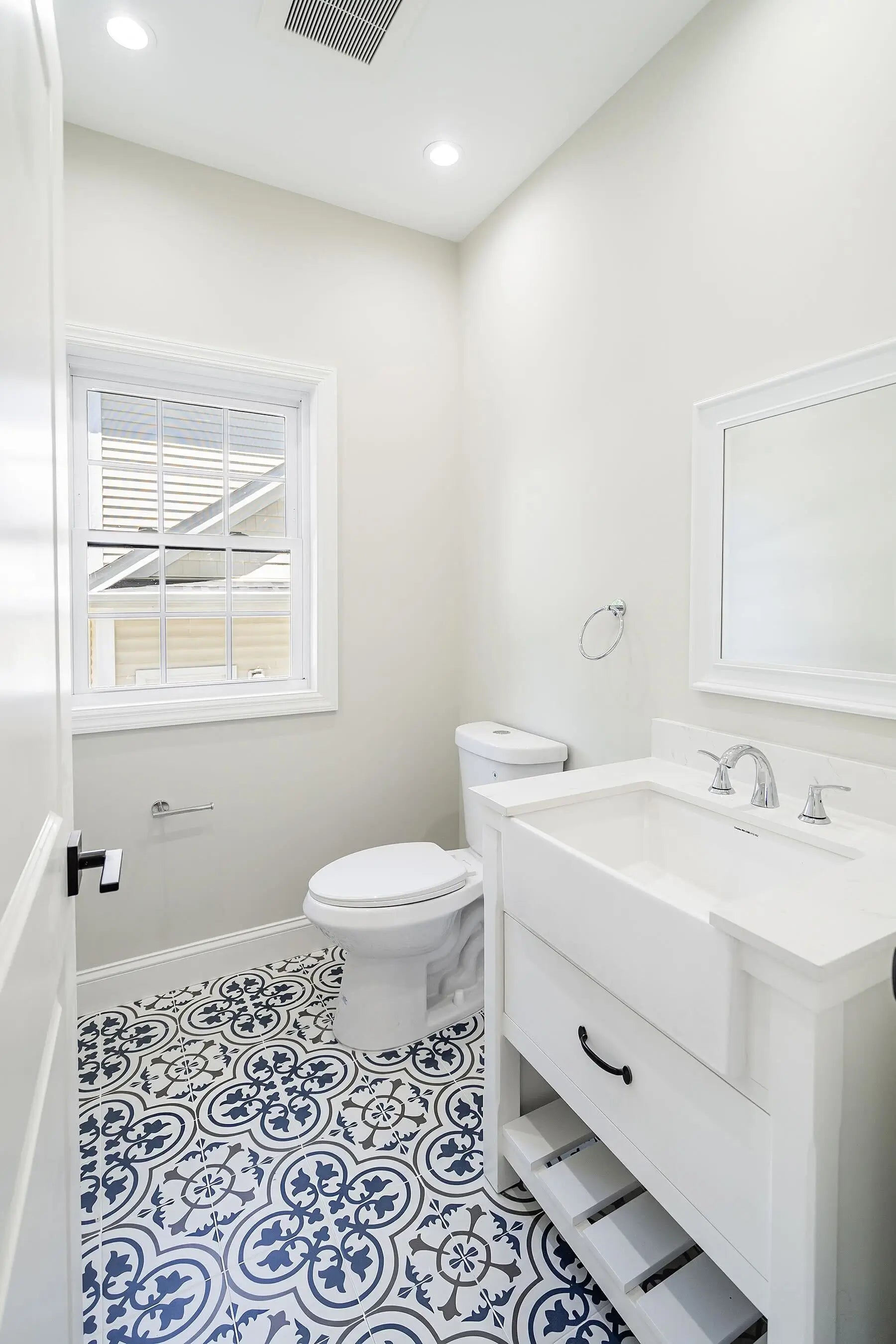 Bathroom with white vanity, toilet, and patterned blue and white floor tiles. Gallery - Quality Home Distribution