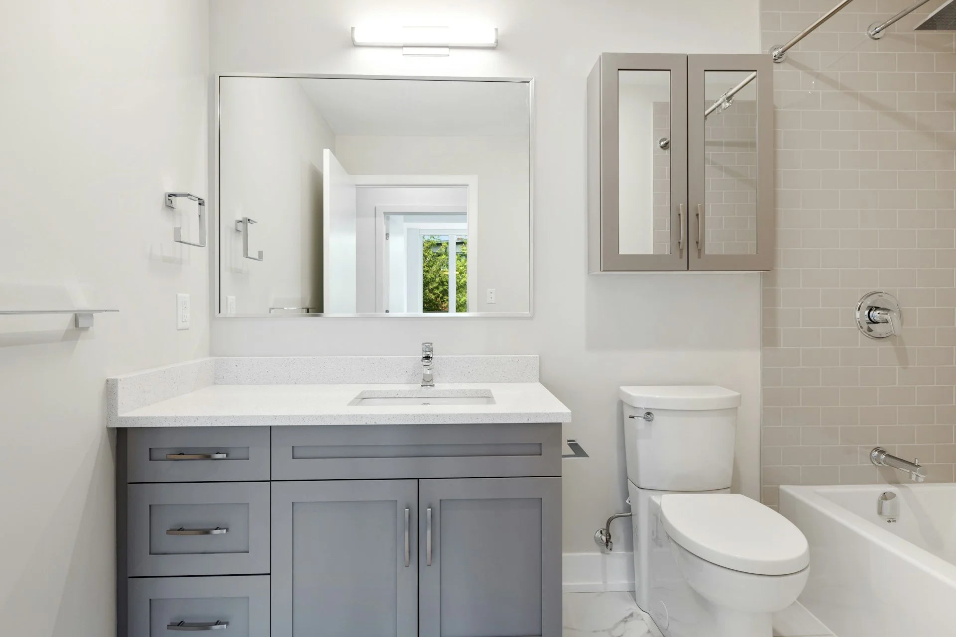 Modern bathroom with gray vanity, white toilet, and bathtub. Gallery - Quality Home Distribution